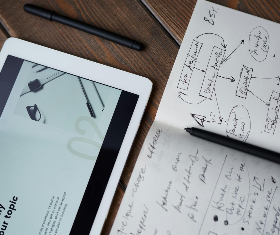A tablet, note book with some handwritten text, and a pencil, on a desk